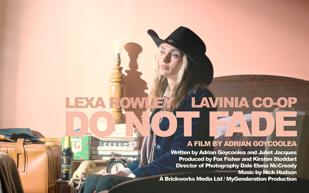 Poster. Lexa Rowley sits on the edge of the bed in a black cowboy hat and velvet jacket, beside a lamp with a bare bulb, a stack of books, a telephone and an alarm clock. Title: Do Not Fade.